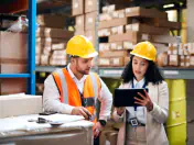 Two people in hard hats look at a clipboard