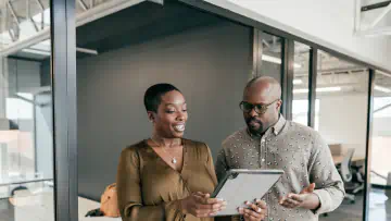 Two office workers examine a handheld tablet