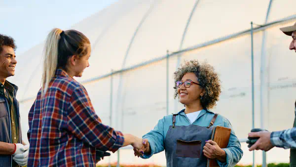 Agricultural workers shake hands in front of a greenhouse